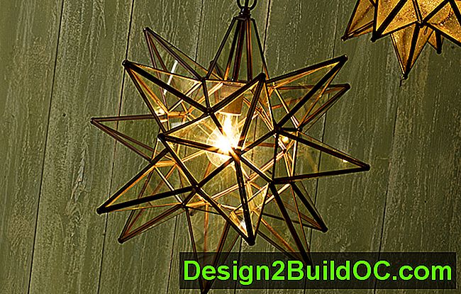 un vetro trasparente con una luce moraviana a sospensione a forma di stella appesa a un muro verde di stecche di legno dall'aspetto invecchiato