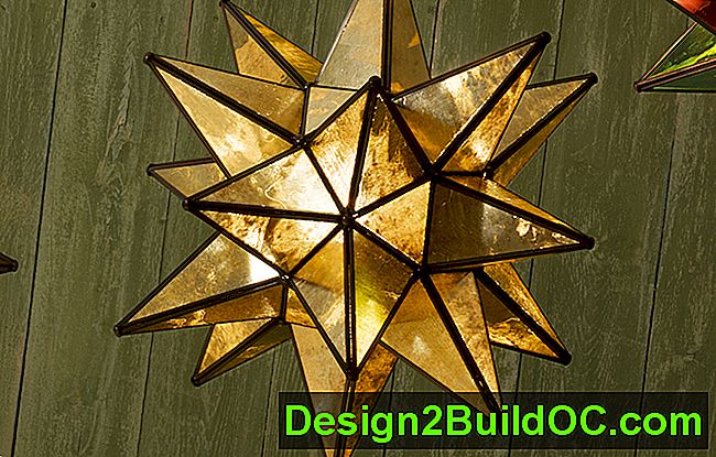 una lampada a sospensione con stella moraviana a 18 punte in oro invecchiato appesa a un muro verde con stecche di legno