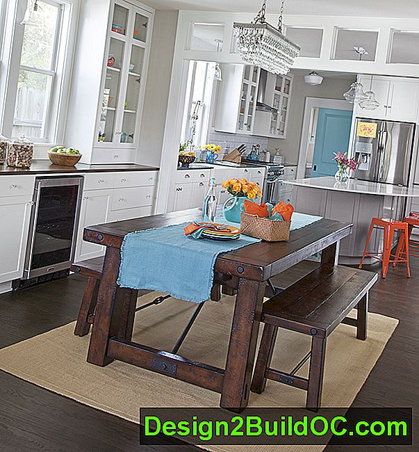 hvidt køkken med transoms, en grå køkkenø med orange metalstole, rustik stil spisebord en lyseblå bordløbere og rustfrit stål apparater