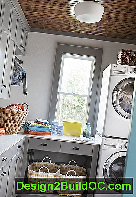 vaskerum bag bagblåmalede glidende lomme dør ud køkken, grå frysere med indbygget opbevaring, stablede vaskeautomater, et vindue og en skole-house stil vedhæng lys på et træ loft